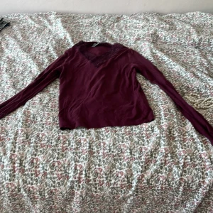 Vinröd långärmad topp med spets Gina Tricot - Vinröd långärmad topp från Gina Tricot med snygg v-ringning och spetsdetaljer runt halsen. Mjuk och skön, perfekt för dig som gillar en enkel men ändå lite extra look. Passar till jeans eller kjol för en chill vibe. Säljer pga av att den är lite liten för mig men använd fåtalsgånger