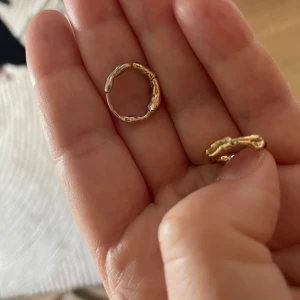 Organiska guldiga örhängen hoops  - Säljer ett par unika örhängen i guldtonad metall med organiskt, ojämnt formad yta. Från pilgrim De är små, runda hoops med en cool, handgjord känsla som sticker ut. Perfekta för dig som gillar minimalistiska men ändå speciella smycken. Det fins en skiftning i guldplateringen där den burjat skava lite men syns knappt se bilder 