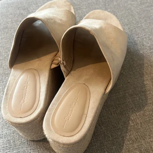 Beige platåsandaler från Bershka - Snygga beige sandaler från Bershka med bred rem över foten och hög platåsula i flätad stil. Ovandelen är i mockaliknande material och sulan har en trendig espadrille-look. Perfekta för sommarens alla outfits.