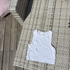 Vit ribbat linne Pull&Bear - Säljer en vit ribbad linnetopp från Pull&Bear. Toppen är ärmlös med rund halsringning och croppad passform, perfekt för varma dagar. Enkel och stilren design som funkar till allt. Materialet är mjukt och stretchigt för extra komfort. Passar även  S