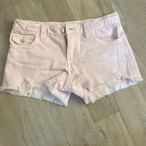 Ljusrosa jeansshorts från Gina Tricot - Snygga ljusrosa jeansshorts från Gina Tricot med fransig kant och slitna detaljer. Klassisk femficksmodell med knapp och dragkedja framtill. Perfekta för varma dagar och ger en avslappnad vibe till din outfit. Helt oanvända. Säljer pga att de var för stora. Orginalpris 349kr