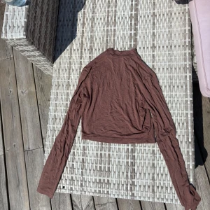 Brun croppad långärmad tröja - Säljer en brun croppad långärmad tröja med enkel design. Tröjan har en hög hals och är tillverkad i ett tunt, mjukt material som passar perfekt till lager-på-lager eller som den är. 