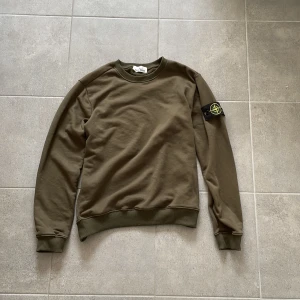 Olivgrön sweatshirt från Stone Island - Säljer en olivgrön sweatshirt från Stone Island med klassisk rund hals och ribbade muddar. Tröjan har den ikoniska Stone Island-patchen på vänster ärm och är tillverkad i mjuk bomull. Perfekt för dig som gillar grisch eller streetwear stilen och snygga detaljer. Som ni ser på bild 5 så funkar det att skanna QR koden. Bara använd en gång - säljer på grund av den inte passar mig som jag hade önskat. 