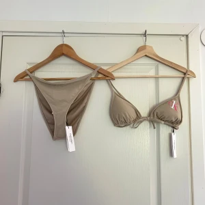 Beige bikini från Calvin Klein - Snygg beige bikini från Calvin Klein med klassisk triangel-bh och smala axelband. Både överdel och underdel har broderad CK-logga i vitt och rosa. Bikinin har knyt framtill på överdelen och är tillverkad i mjuk syntet. Underdel storlek L men tycker den sitter bra på M för att undvika att den ”skär in” på höfterna. Överdel storlek S. Nypris underdel 549 sek, överdel 599 sek. 
