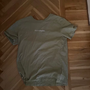 Grön t-shirt från Calvin Klein Jeans - Snygg grön t-shirt från Calvin Klein Jeans med diskret logga tryckt på bröstet. Klassisk passform och rund halsringning, perfekt för en clean och enkel stil. Tillverkad i mjuk bomull som känns skön mot huden.