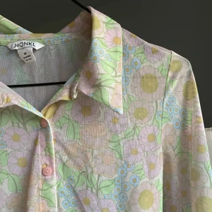 Pastellblommig skjorta från Monki - Supersöt skjorta från Monki i pastelliga färger med blommigt mönster. Skjortan har långa ärmar, klassisk krage och knäppning framtill med rosa knappar. Materialet är genomskinlig. Använts en gång. 