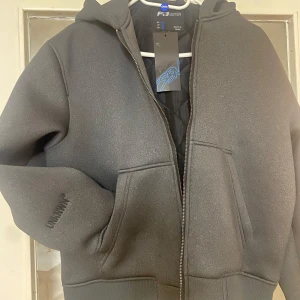 Mörk grå bomberjacka från FB Sister - Mörk grå bomberjacka från FB Sister med huva och dragkedja framtill. Jackan har ribbade muddar, två stora fickor och en clean look med diskret UNKNOWN-brodyr på ärmen. Perfekt för dig som gillar streetstyle och enkel design.