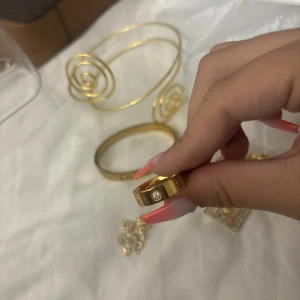 Guldfärgad ring med stenar - Cool guldfärgad ring med blanka stenar och ingraverade detaljer, inspirerad av lyxiga designer. Säljer även matchande armband  ett med spiralform och ett klassiskt bangle. Perfekt för dig som gillar statement-smycken och vill sticka ut.