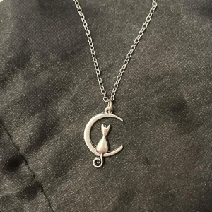 Katt måne halsband silver imitation - En berlock med en katt och en månskära. Trätt på en kortare kedja i silverimitation. Justerbar 35-40 cm.   