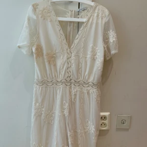 Vit spetsklänning från Zara  - Superfin vit kortklänning från Zara med broderade blommor och transparent mesh. Klänningen har v-ringning, korta ärmar och dragkedja i ryggen. Perfekt för sommarens alla tillfällen och ger en romantisk vibe. Det är storlek L men en M i storlek 