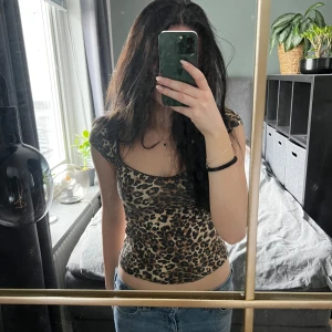 Leopardmönstrad topp från Nelly - Säljer en tight leopardmönstrad topp från Nelly i storlek S. Toppen har korta ärmar, djup rundad urringning och är i stretchigt material som sitter snyggt på kroppen. 