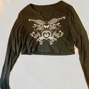 Svart y2k croppad långärmad topp • fjärilar - Svart croppad långärmad topp med snyggt vitt tryck framtill som har fjärilar, hjärtan och blommor i ett symmetriskt mönster. Toppen har en liten v-ringning och sitter tight över kroppen. Perfekt för dig som gillar alternativ stil/y2k/ soft-goth(?). Står att den är strlk L men sitter mer som XS-S-M, stretchigt material dock. Endast använt några fåtal gånger 