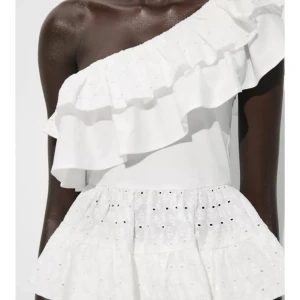 Vit oneshoulder topp  - Superfin vit topp med oneshoulder och bred volangkant. Toppen har broderade detaljer och hålmönster, vilket ger en bohemisk vibe. Sitter snyggt med omlottkänsla och har en luftig passform. PRIS GÅR ATT DISKUTERAS! 