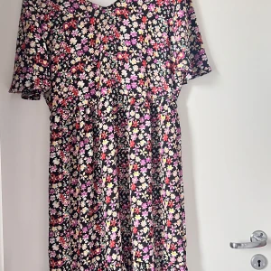 Blommig klänning från JDY - Supersöt kortklänning från JDY med svart botten och färgglatt blommönster i rosa, lila, rött, gult och vitt. Klänningen har korta ärmar och en avslappnad passform, perfekt för vår och sommar. Lätt och skönt material som känns luftigt.