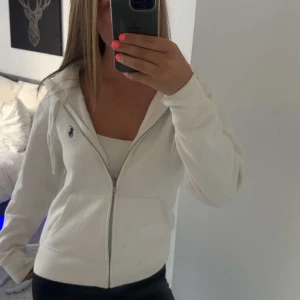 Vit hoodie från Polo Ralph Lauren XS - Vit hoodie från Polo Ralph Lauren med dragkedja och klassisk blå logga på bröstet. Mjuk bomullskänsla, huva med snören och två fickor framtill. Vid funderingar eller intresse kontakta mig gärna!😁