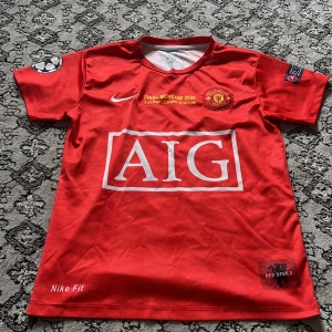 Manchester United Ronaldo 7 Nike tröja - Röd Manchester United fotbollströja från Nike med AIG sponsortryck, Champions League-final 2008-detaljer och klubbmärke. Kortärmad modell med Ronaldo och nummer 7 på ryggen. Materialet är lätt och andas, perfekt för fotboll eller att bära som supporter.