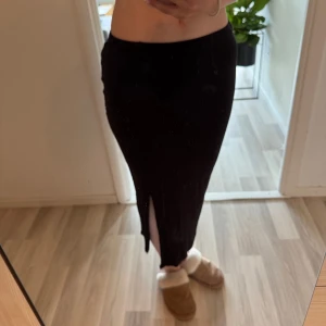Svart långkjol med slits från Lindex - Säljer en svart långkjol från Lindex i storlek S. Kjolen har en snygg slits på sidan som ger en cool vibe och är perfekt att styla med sneakers eller boots. Enkel och stilren design som funkar till många olika looks.