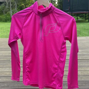 Rosa långärmad träningströja från Röhnisch - Snygg och sportig rosa långärmad träningströja från Röhnisch med halv dragkedja framtill och hög krage. Tillverkad i mjukt och stretchigt syntetmaterial, perfekt för löpning eller gym. Reflekterande logga på bröstet och diskret reflexdetalj på ryggen.