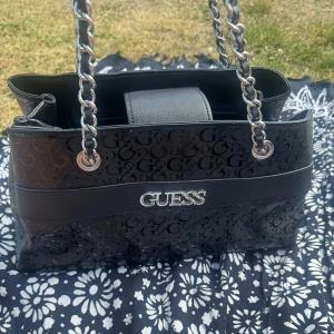 Svart axelväska från Guess med kedja - Snygg svart axelväska från Guess med silverfärgade kedjehandtag. Väskan har flera fack och småfack och dragkedja. Nypris 1900kr i Guess butiken i Barkarby!