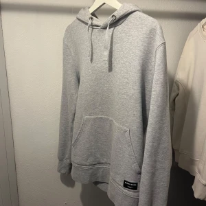 Grå hoodie från Björn Borg - Säljer en stilren ljusgrå hoodie från Björn Borg i mjuk bomullsmix. Tröjan har huva med snörning, stor magficka och ribbade muddar. Perfekt för chill dagar eller när du vill ha en enkel och clean look.