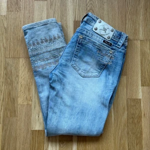 Dam MISS ME Signature Cuffed Skinny Ljusblåa Jeans - MISS ME jeans i modellen Signature Cuffed Skinny och färgen Ljusblå till Dam. OBS! Foder över broderi på insidan av ena jeansbenet har gått upp men gör egentligen ingen större skillnad, kan bara fastnas i när man tar på sig dem men går att limma eller sy fast igen Storlek: 30, Midja: 45 cm Ytterben: 97 cm Benöppning: 16.5 cm Material: 98% Cotton, 2% Elastane.