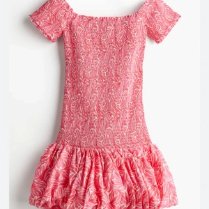 Rosa kortklänning med volang - Supersöt rosa kortklänning med vita mönster och volangig kjol. Smockad överdel och korta ärmar som kan bäras offshoulder. Perfekt för sommarens alla tillfällen, riktigt skön och luftig känsla. INTRESSEKOLL