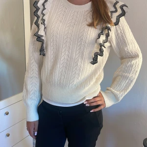 Vit stickad tröja med volangdetaljer från Lindex - Superfin vit stickad tröja med svarta volangdetaljer längs axlarna. Tröjan har ett snyggt mönsterstickat tyg, rund halsringning och långa ärmar. Perfekt för dig som vill ha något unikt och trendigt i garderoben! Är från Lindex barnavdelning 