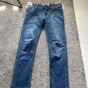 Blå jeans från Jacob Cohën, stl 32 - Snygga blå jeans från Jacob Cohën i klassisk modell med raka ben och normal passform. Jeansen har fem fickor, kontrastsömmar och patch med logga bak i midjan. Perfekta för dig som gillar stilrena och tidlösa jeans.