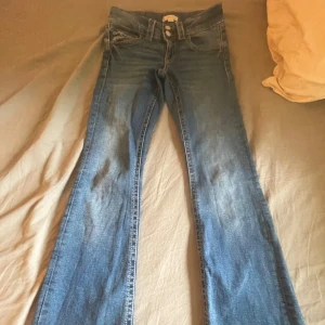 Blå bootcut jeans från Gina Tricot - Snygga blå jeans från Gina Tricot i klassisk bootcut-modell. Jeansen har normalhög midja, två knappar framtill och raka bakfickor. Tillverkade i mjukt denim med lätt slitningar för en cool look.