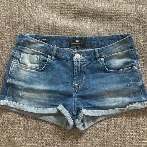 Blå jeansshorts från LTB - Snygga blå jeansshorts från LTB med klassisk femficksdesign, uppvikta benslut och slitna detaljer framtill. Shortsen har normal passform och bälteshällor. Midjemått rakt över 38cm💕