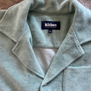 Mintgröna frottéshorts från Nikben - Snygga gröna shorts från Nikben i mjuk frotté. Strl 14 men passar 11-13 år mer. Shortsen har elastisk midja med snörning och en bakficka med liten Nikben-logga. Perfekta för chill dagar eller efter badet. Matcha med skjortan för en clean look. Använda 2 ggr så mycket fint skick. 300 för hela setet.