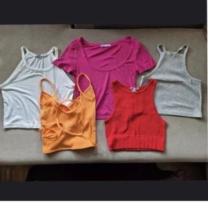 Fem ribbade croppade linnen i mixade färger - Säljer ett paket med fem ribbade croppade linnen i olika färger: vitt, grått, rött, orange och cerise. Alla är ärmlösa och har olika halsringningar, vissa med smala axelband och andra med bredare. Perfekta för sommaren och att styla lager på lager.