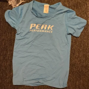 Blå Peak Performance t-shirt - Snygg ljusblå t-shirt från Peak Performance med vit logga tryckt på bröstet. Klassisk rund halsringning och korta ärmar. Perfekt för dig som gillar sportig och enkel stil.