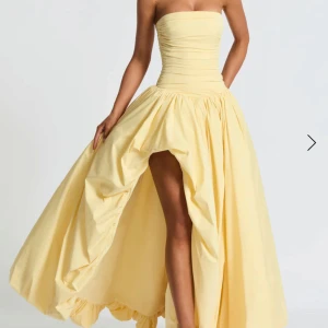 Ljusgul långklänning med snörning - Superfin ljusgul långklänning med axelbandslös design och markerad midja. Klänningen har snörning i ryggen, draperad överdel och en dramatisk slits framtill. Kjolen är voluminös och ger en riktigt sagolik känsla. Perfekt för dig som vill sticka ut! nypris 2600 från babyboo