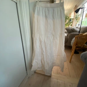 Vit långkjol från Lindex - Säljer en vit långkjol från Lindex i storlek 158. Kjolen har resår i midjan och är tillverkad i mjuk bomull. Den har en luftig och flowy känsla med volangdetalj nedtill, perfekt för varma dagar.