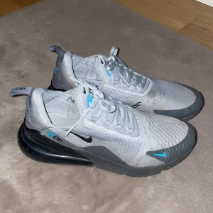 Nike Air Max 270 i grått och blått - Nike Air Max 270 sneakers i ljusgrå mesh med svarta och blå detaljer. Skorna är använda flitigt vilket resulterar i priset, hör gärna av er vid frågor.