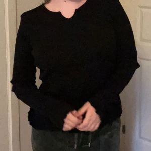 Svart ribbad långärmad tröja Lindex - Svart långärmad tröja från Lindex med ribbad struktur och lätt vågiga kanter vid ärmslut och nederkant. Tröjan har en liten v-ringning vid halsen och sitter tajt mot kroppen. Perfekt för dig som gillar en enkel men snygg stil.