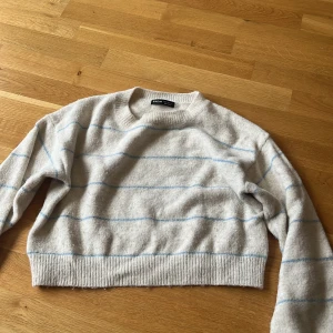 Randig stickad tröja från SHEIN - Mysig ljusgrå stickad tröja från SHEIN med tunna blå ränder. Tröjan har en croppad passform, rund halsringning och långa ärmar. Perfekt för dig som gillar en enkel men ändå trendig look.