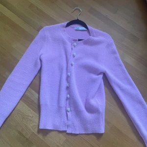 Ljuslila kofta från Zara med pärlknappar - Superfin ljuslila kofta från Zara med långa ärmar och söta pärlknappar framtill. Koftan har en rund halsringning och är stickad i ett mjukt material som känns skönt mot huden. Perfekt att slänga över en topp för en söt look.