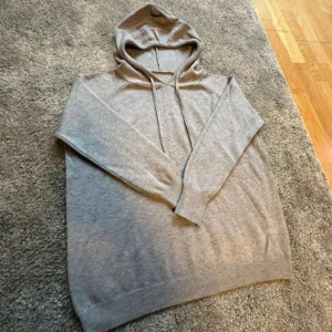 Grå merinoull hoodie - Säljer en supermjuk och bekväm grå hoodie i merinoull. Perfekt för kyliga dagar med sin avslappnade passform och långa ärmar. Säljer den på grund av att den inte passar så bra.