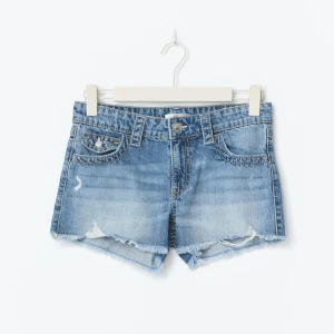 Blå jeansshorts med fransig kant - Snygga blå jeansshorts med fransig kant och slitna detaljer. Klassisk femficksmodell med knapp och dragkedja framtill. Perfekta för varma dagar och en avslappnad stil. Helt ny utan prislapp🌼💘