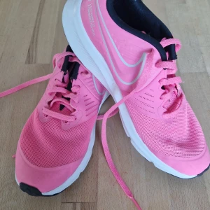 Nike Star Runner rosa sneakers - Snygga Nike Star Runner sneakers i en stark rosa färg med vita detaljer och svart insida. Skorna har ventilerande mesh, klassisk snörning och en vit sula med svart yttersula. Perfekta för dig som gillar färg och vill sticka ut på träningen.
