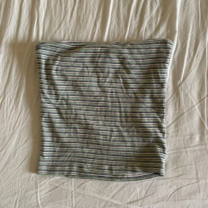 Randig bandeau tubtopp i bomull - Säljer en randig bandeau tubtopp i mjuk bomull. Toppen har tunna horisontella ränder i svart, vit, grön och grå. Perfekt att styla med jeans eller kjol för en chill look. Ärmlös och axelbandslös design som sitter snyggt på plats.