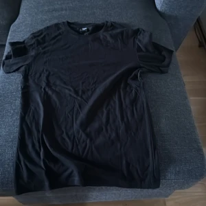 Svart slim fit t-shirt från FSBN - En stilren svart t-shirt från FSBN i slim fit-modell. Klassisk rund halsringning och korta ärmar. Tillverkad i mjuk bomull som känns skön mot huden. Perfekt basplagg för en clean och enkel look.
