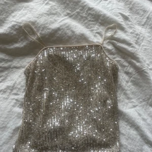 Glittrig paljett-tubtopp i silver - Säljer en snygg glittrig tubtopp med tunna axelband.  Den har en croppad passform. Kan användas som kjol också!