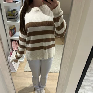 Randig stickad tröja i beige och vitt - Säljer en mysig stickad tröja med breda beige och vita ränder. Tröjan har slits vid ärmen och längst ner som man ser på sista bilden 💞