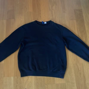 Svart sweatshirt från H&M Divided - En enkel svart sweatshirt från H&M Divided. Tröjan har rund halsringning och långa ärmar. Perfekt basplagg som passar till många olika stilar. Mjuk och bekväm med ribbade muddar vid ärmslut och nederkant.