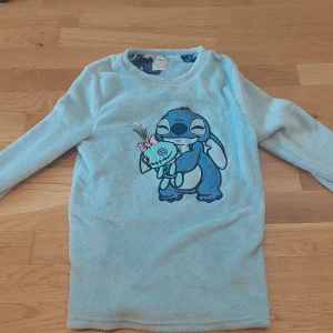 Ljusblå fleece-tröja med Stitch från Disney helt ny! - Supermjuk ljusblå fleece-tröja från Disney med stort tryck av Stitch som kramar en docka på framsidan. Tröjan har långa ärmar och rund hals. Perfekt för dig som älskar Disney och vill ha något mysigt att ha på dig. Fick med den i ett sätt med ett par byxor men ville inte ha tröjan!