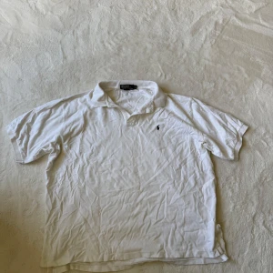 Vit pikétröja från Polo Ralph Lauren XXL - Säljer en vit pikétröja från Polo Ralph Lauren med korta ärmar och krage. Tröjan har en liten broderad logga på bröstet och är tillverkad i bomull. 