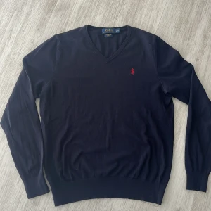 Mörkblå merinoullströja från Polo Ralph Lauren - Säljer en mörkblå långärmad tröja från Polo Ralph Lauren i merinoull. Tröjan har v-ringning och en röd broderad logga på bröstet. Slim fit-modell som passar perfekt till många tillfällen.